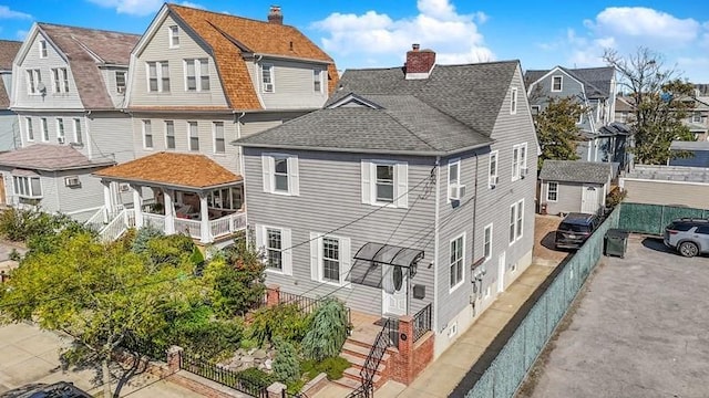 back of property featuring a chimney, a shingled roof, fence, a residential view, and driveway