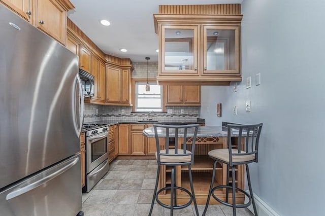 kitchen with brown cabinets, dark countertops, decorative backsplash, appliances with stainless steel finishes, and a sink