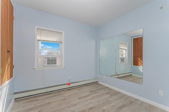 empty room featuring a baseboard heating unit, wood finished floors, and baseboards