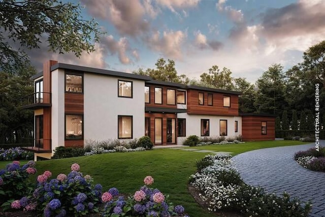 back of property at dusk featuring a lawn, a balcony, and stucco siding