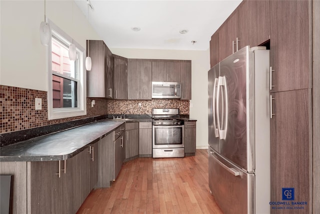 kitchen with dark countertops, light wood-style flooring, appliances with stainless steel finishes, backsplash, and a sink