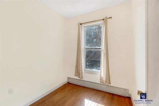 empty room featuring light wood-style flooring, a baseboard heating unit, and baseboards