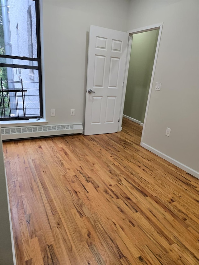 spare room with a baseboard radiator, wood finished floors, and baseboards