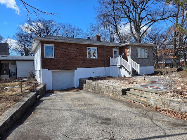 single story home featuring a garage, brick siding, a chimney, and aphalt driveway