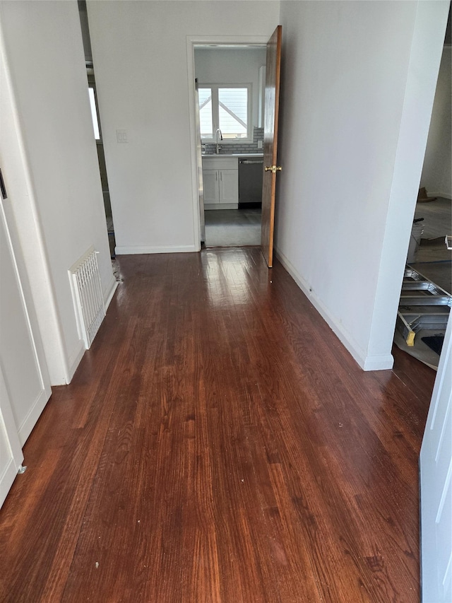 hallway featuring dark wood-style floors, baseboards, visible vents, and a sink