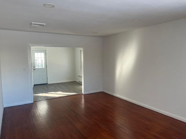 unfurnished room featuring radiator heating unit, wood finished floors, visible vents, and baseboards