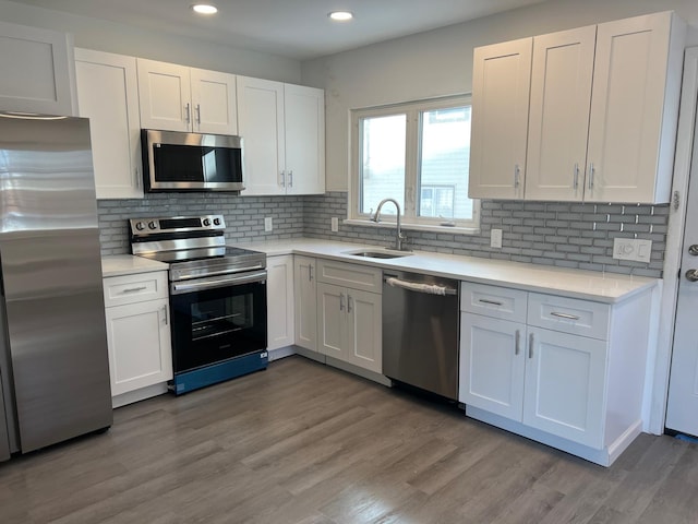 kitchen with white cabinets, appliances with stainless steel finishes, wood finished floors, light countertops, and a sink