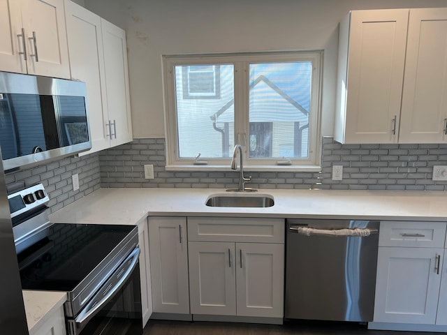 kitchen with appliances with stainless steel finishes, a sink, white cabinets, and tasteful backsplash