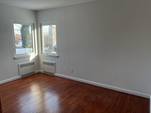 spare room with baseboards, wood finished floors, and radiator