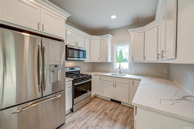 kitchen featuring light stone counters, appliances with stainless steel finishes, white cabinetry, a sink, and light wood-type flooring