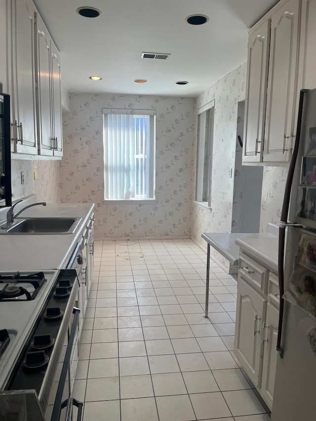 kitchen featuring light tile patterned flooring, a sink, stainless steel gas range, freestanding refrigerator, and wallpapered walls