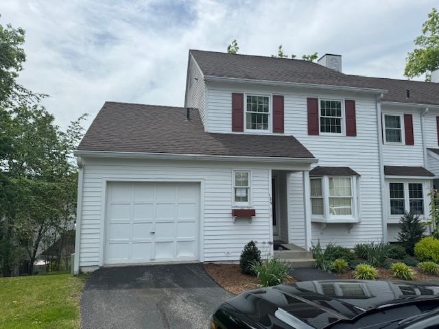 view of front of home featuring a garage, driveway, a chimney, and roof with shingles