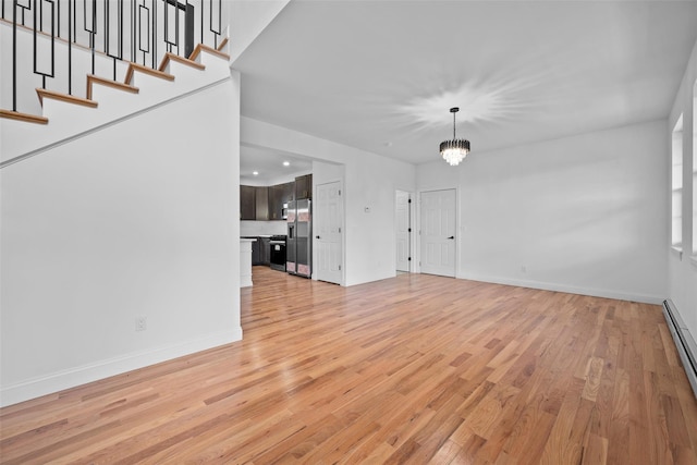 unfurnished living room with light wood-style floors, a baseboard radiator, a notable chandelier, and stairs