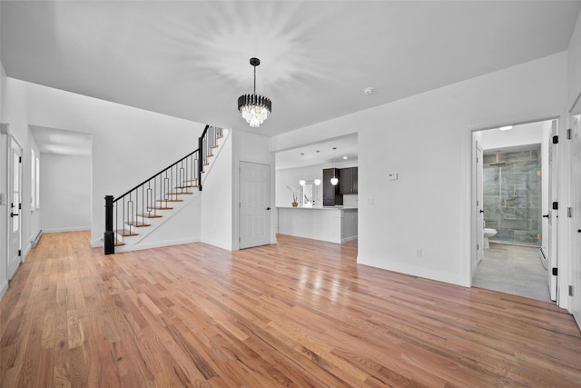 unfurnished living room featuring light wood-style floors, baseboards, an inviting chandelier, and stairs