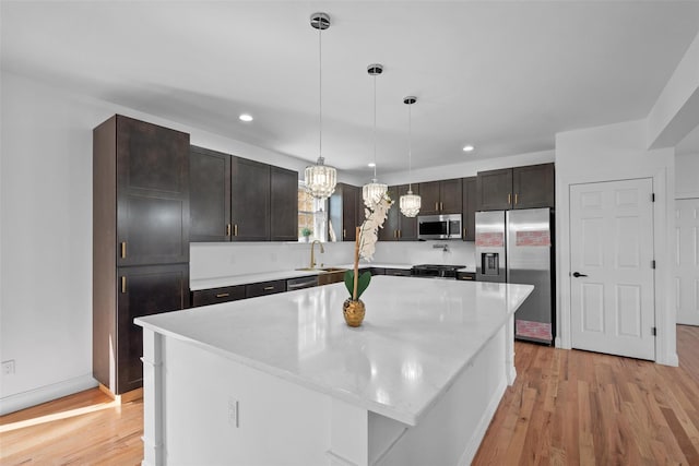 kitchen with pendant lighting, stainless steel appliances, a sink, dark brown cabinetry, and light wood-type flooring