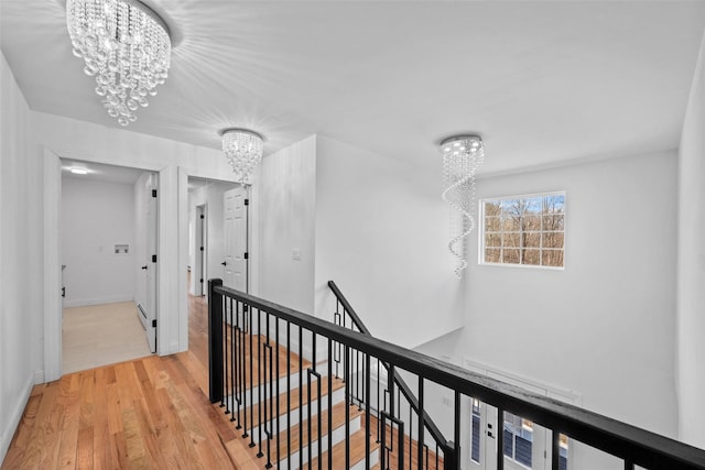 corridor with light wood-type flooring, baseboards, a notable chandelier, and an upstairs landing