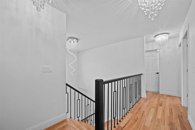 hall featuring baseboards, wood finished floors, an upstairs landing, and a notable chandelier