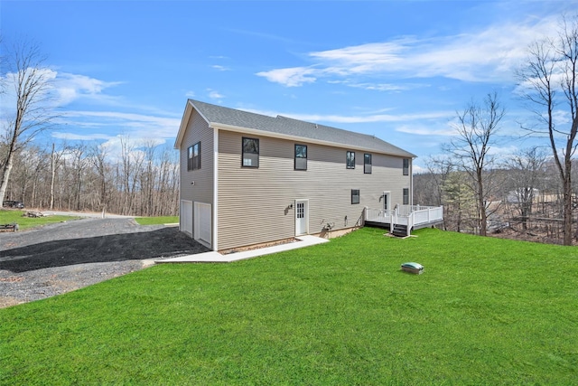 back of house with a garage, a lawn, driveway, and a wooden deck