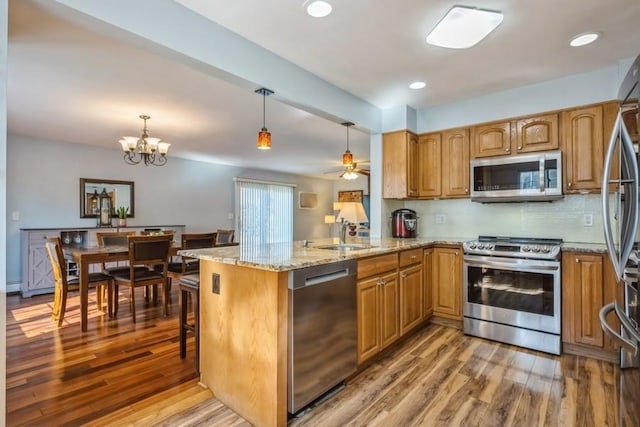 kitchen with brown cabinetry, a peninsula, stainless steel appliances, and a sink