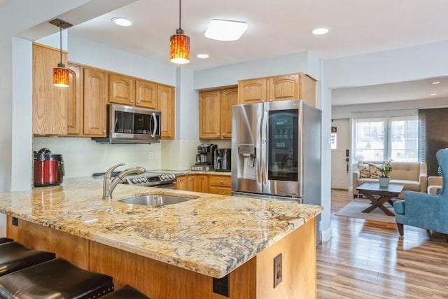 kitchen with light stone countertops, a peninsula, a sink, appliances with stainless steel finishes, and decorative light fixtures