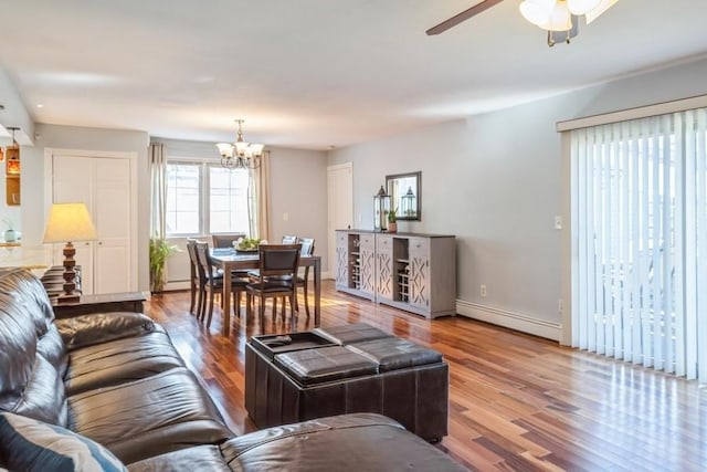 living area featuring baseboard heating, ceiling fan with notable chandelier, baseboards, and wood finished floors