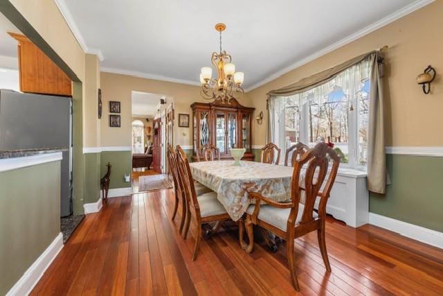 dining room with ornamental molding, baseboards, hardwood / wood-style floors, and an inviting chandelier