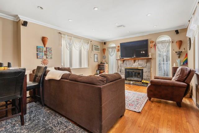 living area featuring a stone fireplace, recessed lighting, hardwood / wood-style flooring, and crown molding