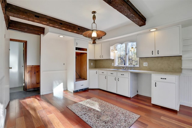 kitchen featuring wood finished floors, white cabinets, light countertops, beamed ceiling, and decorative light fixtures