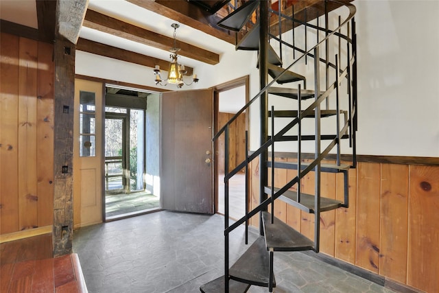 foyer with a chandelier, wood walls, stairway, beam ceiling, and stone finish flooring