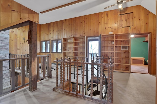 hallway featuring a wealth of natural light, vaulted ceiling, wood walls, and an upstairs landing