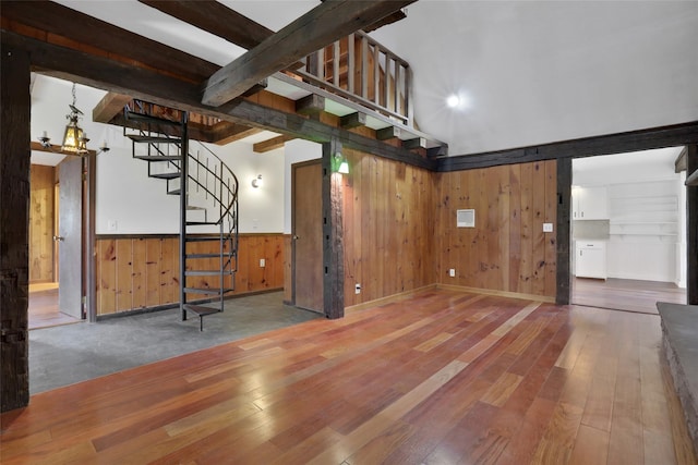 unfurnished living room with hardwood / wood-style flooring, stairway, beamed ceiling, and wainscoting