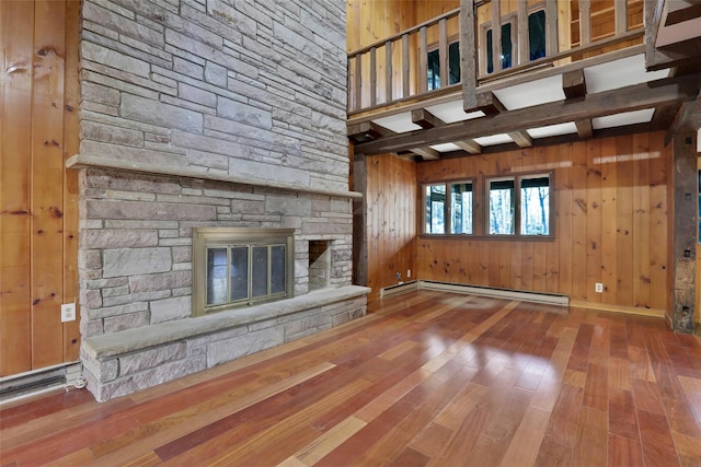 unfurnished living room featuring a fireplace, baseboard heating, wooden walls, wood finished floors, and beamed ceiling