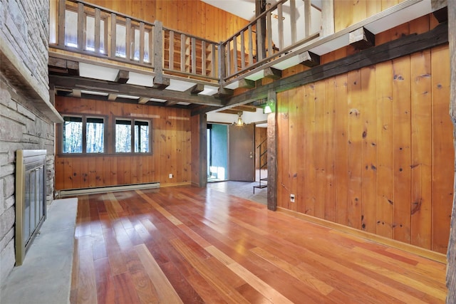 unfurnished living room with a fireplace, a baseboard radiator, a high ceiling, wooden walls, and hardwood / wood-style floors