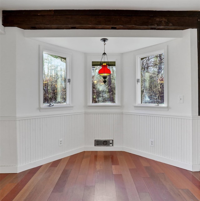 unfurnished dining area featuring hardwood / wood-style floors, visible vents, beam ceiling, and a wainscoted wall