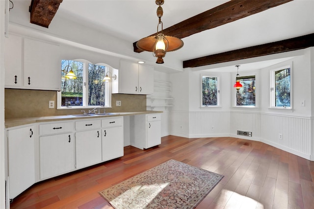 kitchen featuring a healthy amount of sunlight, a sink, beamed ceiling, and wood finished floors