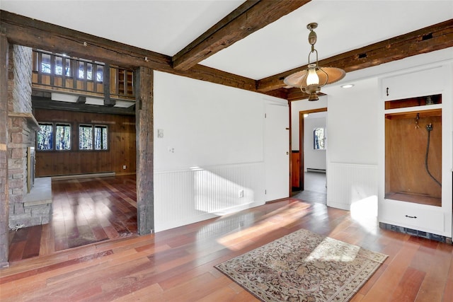 interior space with a wainscoted wall, wood-type flooring, a baseboard heating unit, and beam ceiling