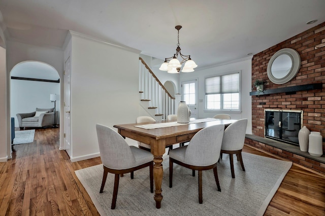 dining space with arched walkways, crown molding, a brick fireplace, light wood-type flooring, and baseboards