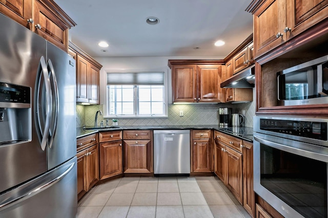 kitchen featuring light tile patterned floors, under cabinet range hood, stainless steel appliances, a sink, and decorative backsplash