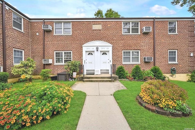 view of front of home with a wall mounted air conditioner, brick siding, and a front lawn