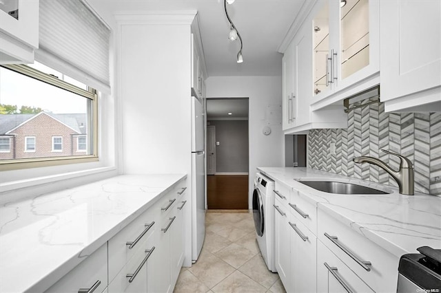 kitchen featuring a sink, white cabinets, decorative backsplash, washer / clothes dryer, and glass insert cabinets