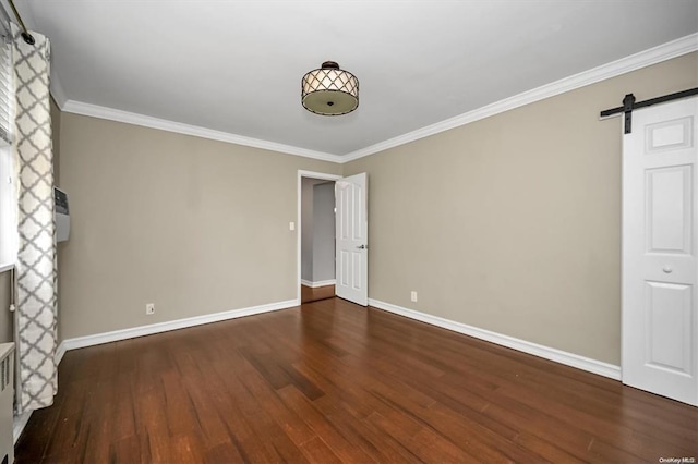 spare room with wood finished floors, crown molding, baseboards, and a barn door