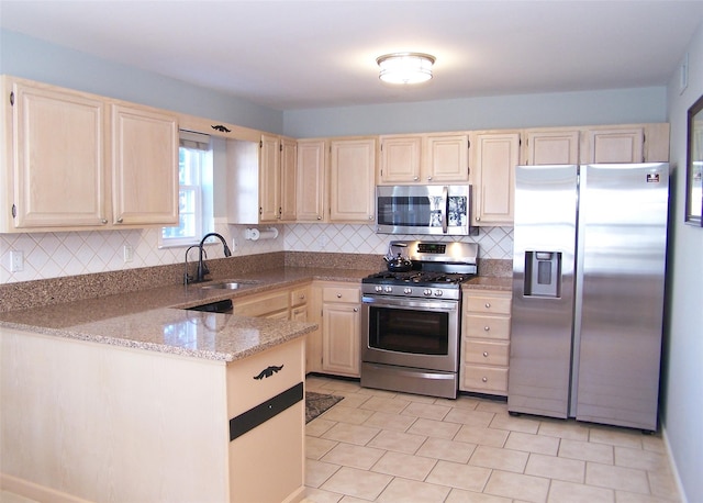 kitchen with light stone counters, a peninsula, a sink, stainless steel appliances, and backsplash