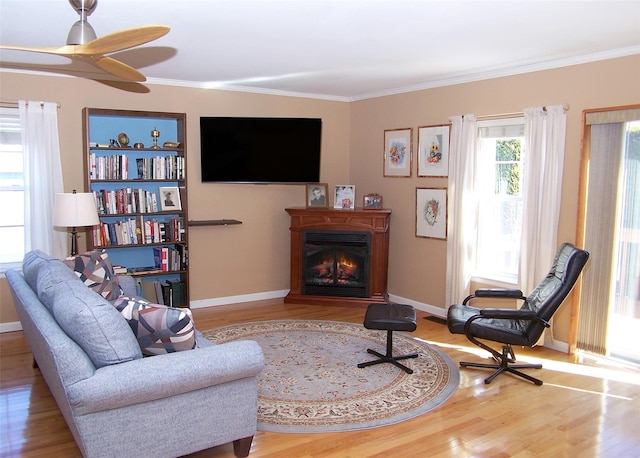 living area featuring a warm lit fireplace, baseboards, wood finished floors, and crown molding