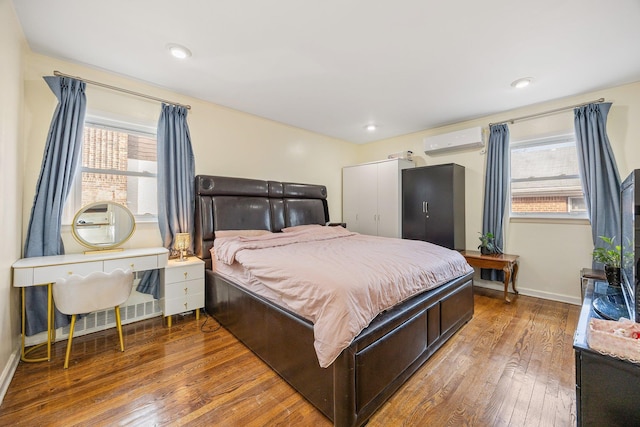 bedroom with multiple windows, a wall unit AC, wood-type flooring, and baseboards