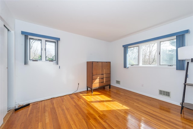 unfurnished bedroom featuring hardwood / wood-style floors, multiple windows, and visible vents