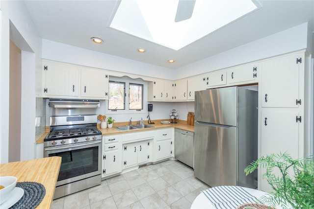 kitchen with range hood, light countertops, appliances with stainless steel finishes, white cabinets, and a sink