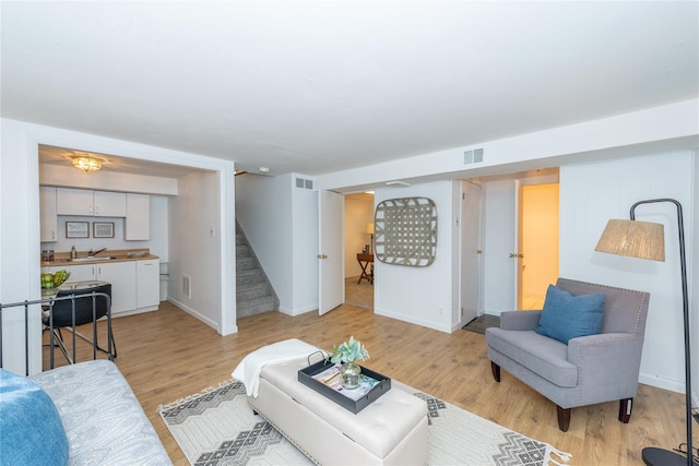 living area with baseboards, visible vents, stairway, and light wood finished floors