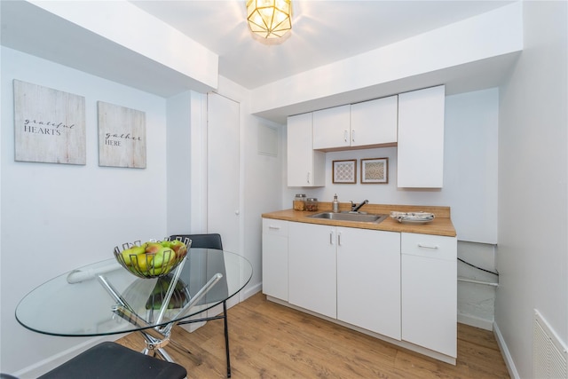 kitchen with light wood-style flooring, a sink, visible vents, baseboards, and white cabinetry