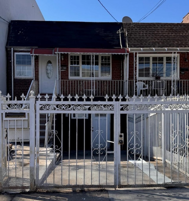 view of front facade featuring a fenced front yard, roof with shingles, a gate, a porch, and brick siding