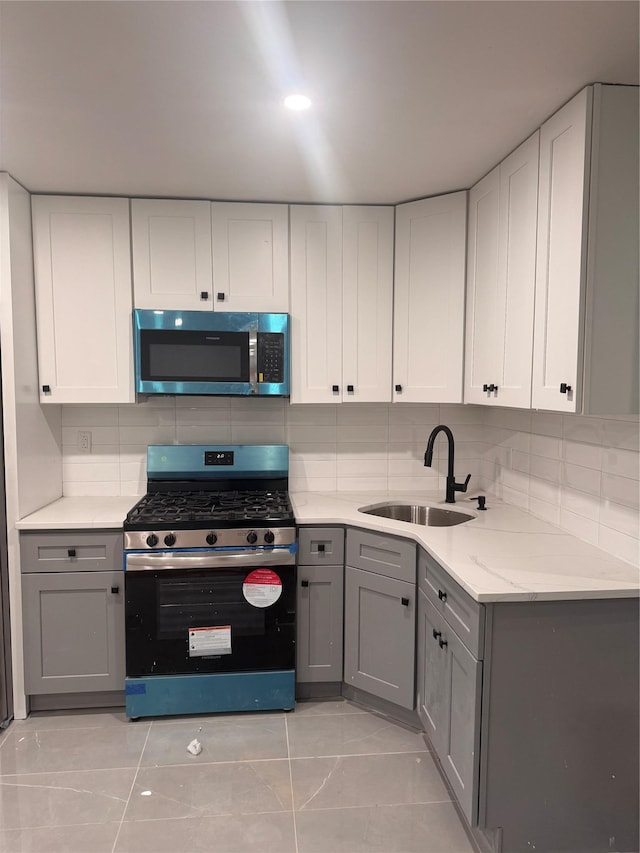 kitchen featuring decorative backsplash, stainless steel appliances, gray cabinetry, white cabinetry, and a sink